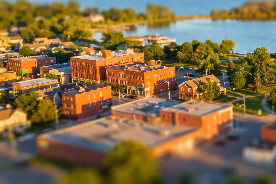 Tilt-shift miniature of red-brick town buildings and trees beside a calm blue lake