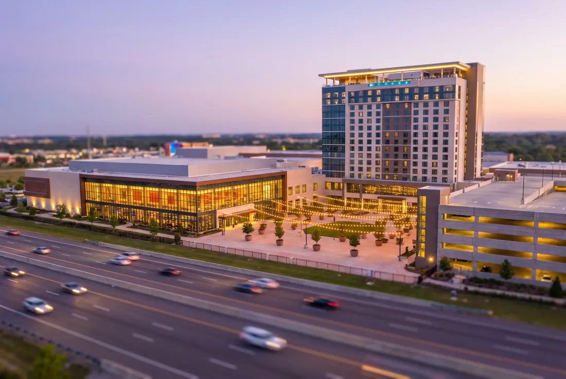 Vue miniature façon tilt-shift d'un grand complexe de divertissement à façade vitrée, avec une tour d'hôtel, au bord d'une autoroute achalandée au crépuscule