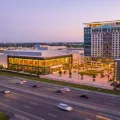 Vue miniature façon tilt-shift d'un grand complexe de divertissement à façade vitrée, avec une tour d'hôtel, au bord d'une autoroute achalandée au crépuscule